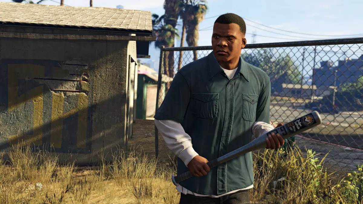 Franklin Clinton, jeune homme en chemise verte et batte de baseball à la main, dans une ruelle grillagée d'un quartier sud de Los Santos, palmiers et maison délabrée en arrière-plan