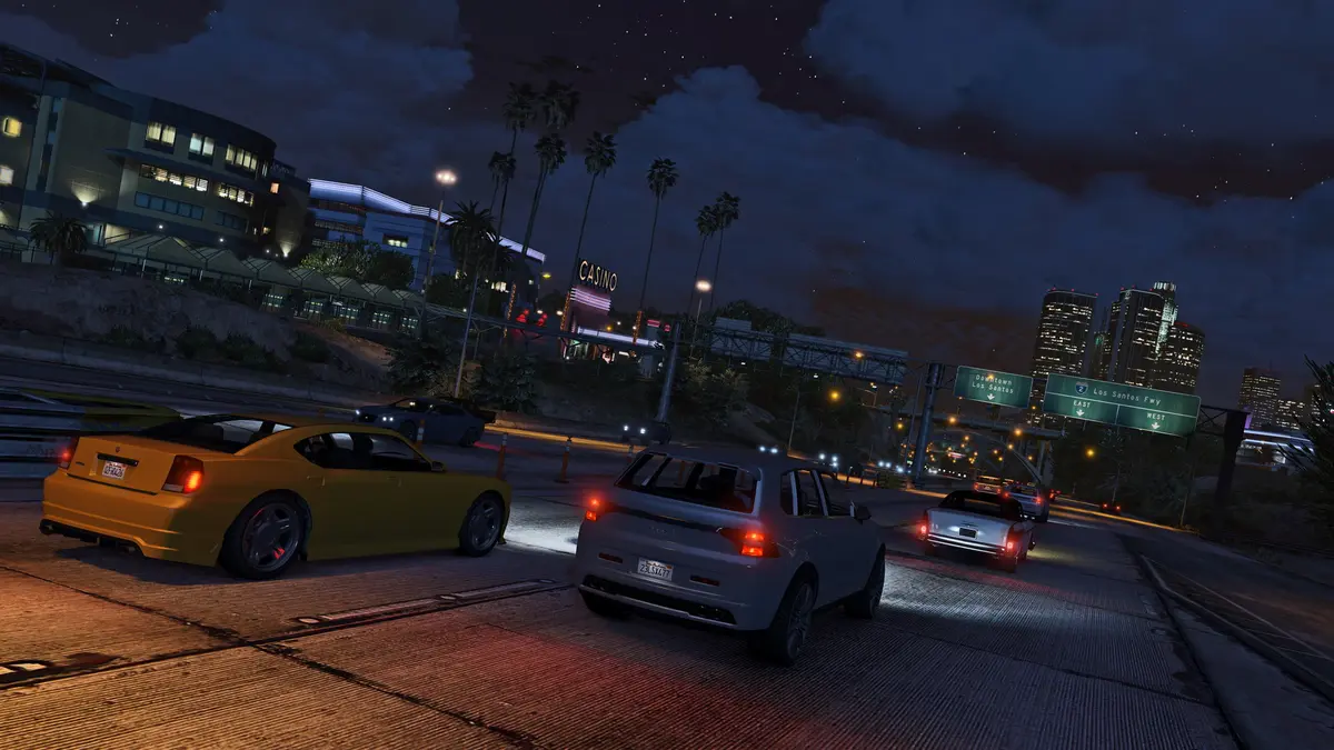 Rue de Los Santos la nuit dans GTA 5, feux arrière rouges des voitures, gratte-ciel illuminés au loin, ambiance de poursuite urbaine