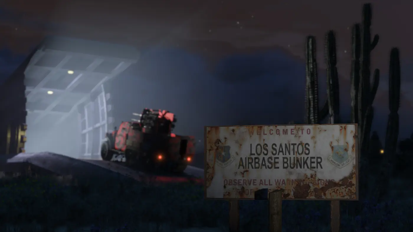 Entrée d'un bunker souterrain de GTA Online la nuit, sa porte blindée massive ouverte, un véhicule armé qui en sort, un panneau rouillé et des cactus dans le désert