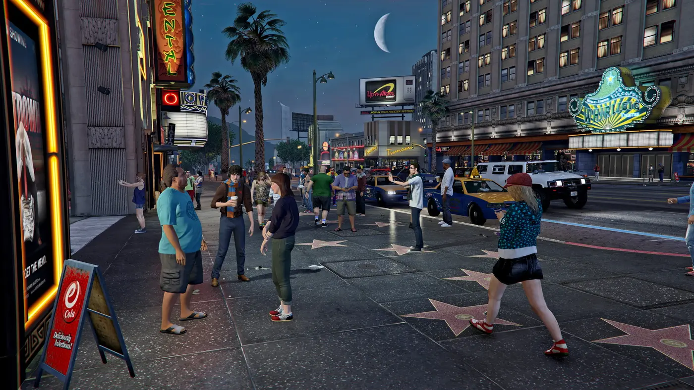 Foule de piétons sur le Vinewood Boulevard de Los Santos la nuit, étoiles du Walk of Fame au sol, enseignes néon de cinémas et gratte-ciel illuminés, dans GTA 5