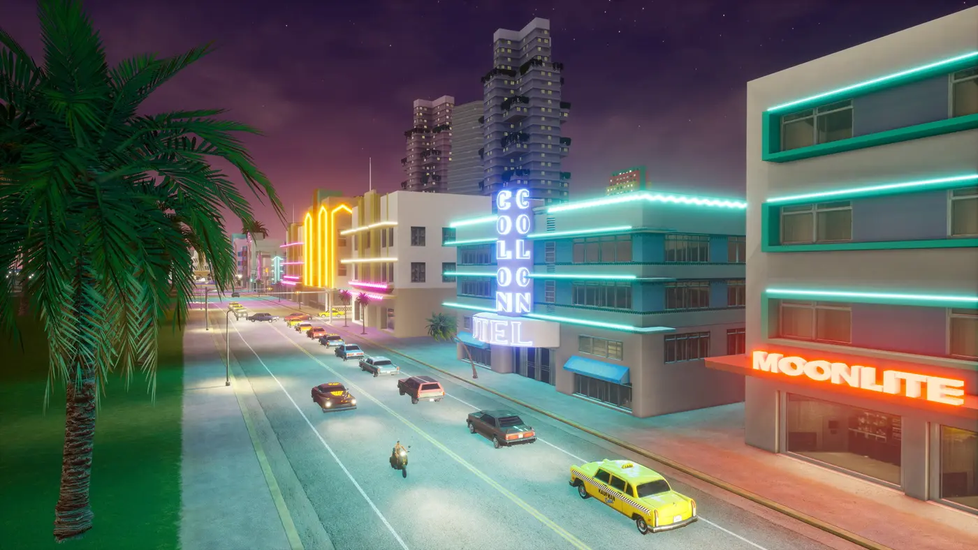 Boulevard de Vice City la nuit, néons turquoise et roses des hôtels art déco, un taxi jaune et des voitures qui roulent sur l'avenue, une moto au premier plan, dans le remaster Definitive Edition