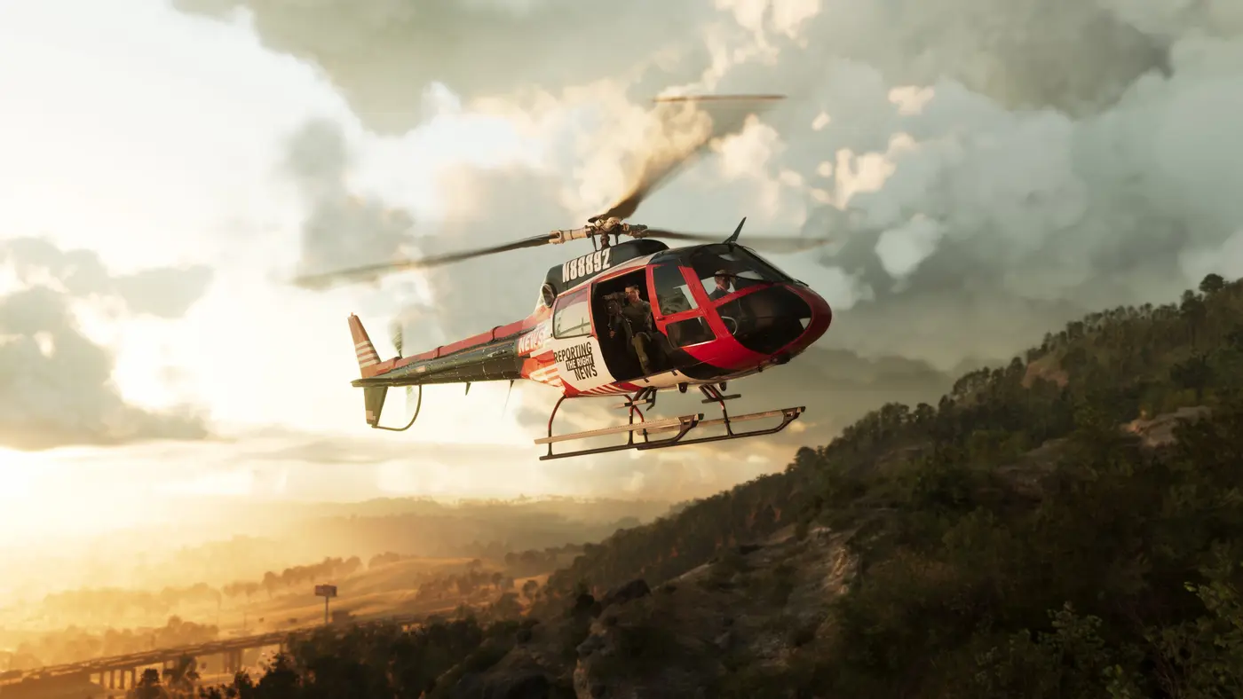 Vue aérienne au coucher de soleil d'un hélicoptère de presse survolant les collines boisées de Mount Kalaga dans GTA VI, une autoroute traversant la vallée en contrebas, lumière dorée et gros nuages